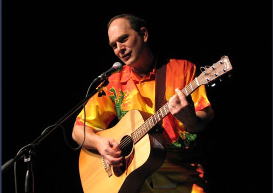 A man in yellow shirt playing guitar on stage.