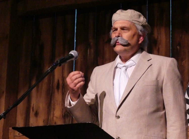 A man with a mustache and beard is speaking at a podium.