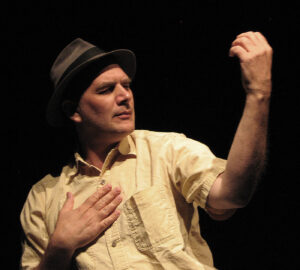 A man in a hat and shirt holding his hands up.