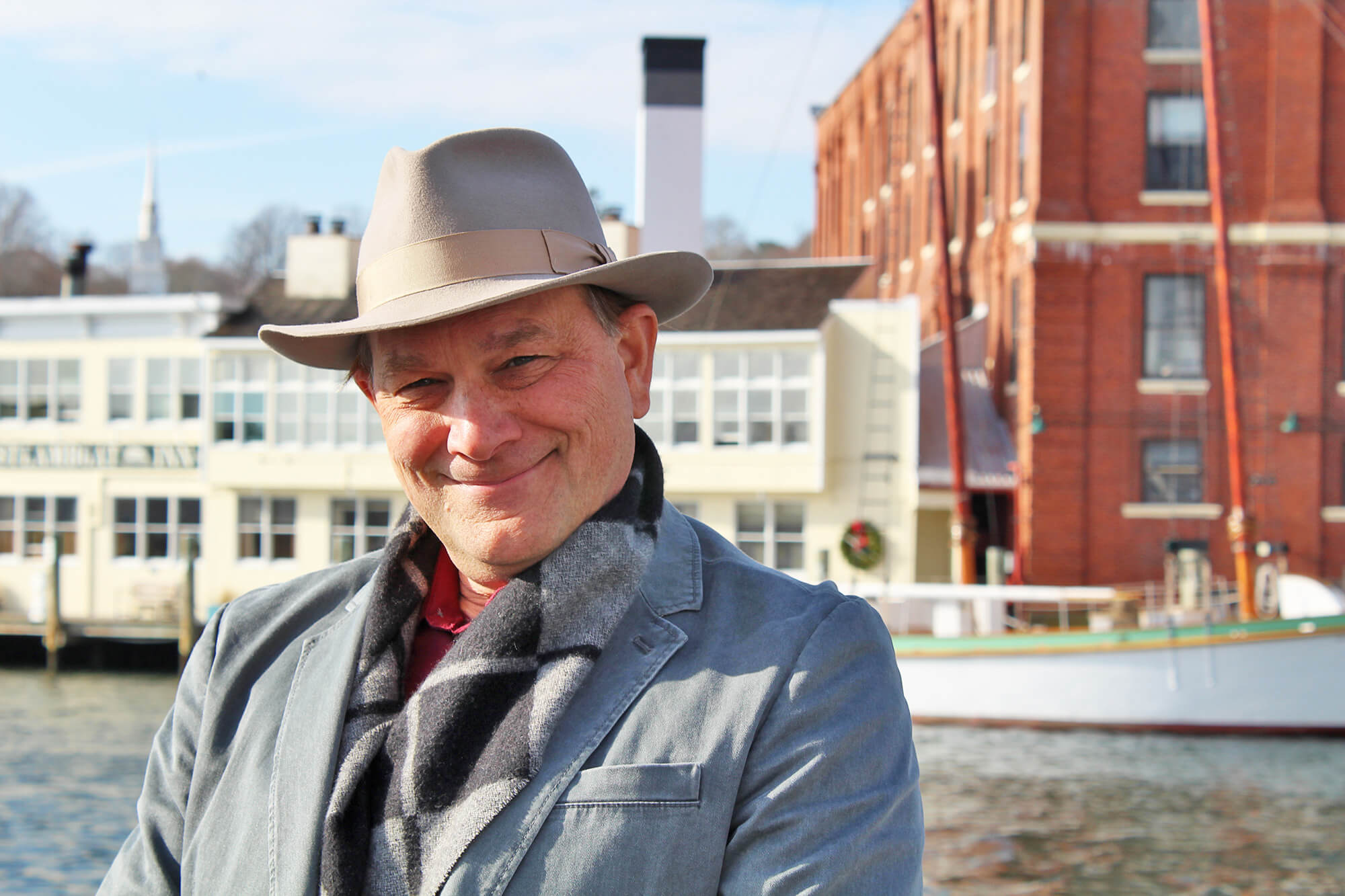 A man in a hat and jacket standing next to a building.